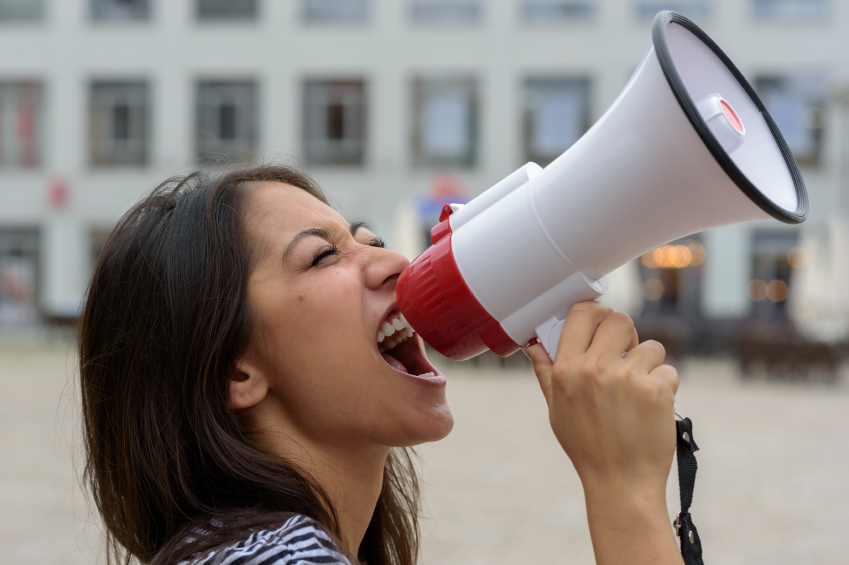 Woman yelling into a bullhorn on an urban street voicing her displaeasure during a protest or demonstration, close up side view of her face