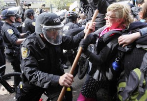 A Seattle police officer wearing riot gear tangles with a woman during May Day demonstrations that went violent in downtown Seattle